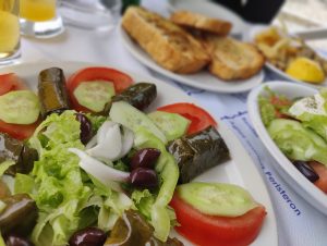 A plate of dolmades, Greek salad, bread and beer on a table.